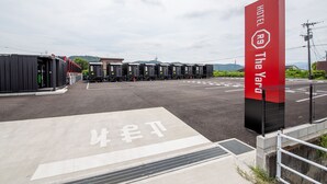 A hotel entrance with a red sign, a parking lot, and a row of luggage carts. - HOTEL R9 The Yard Uki (Uki)