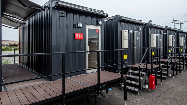 A row of black modular cabins with metal railings and wooden decks, each with a door and a small window. - HOTEL R9 The Yard Uki (Uki)