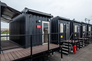 A row of black modular cabins with metal railings and wooden decks, each with a door and a small window. - HOTEL R9 The Yard Uki (Uki)