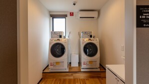 A laundry room with two front-loading washing machines, a small window, and a door. - HOTEL R9 The Yard Uki (Uki)