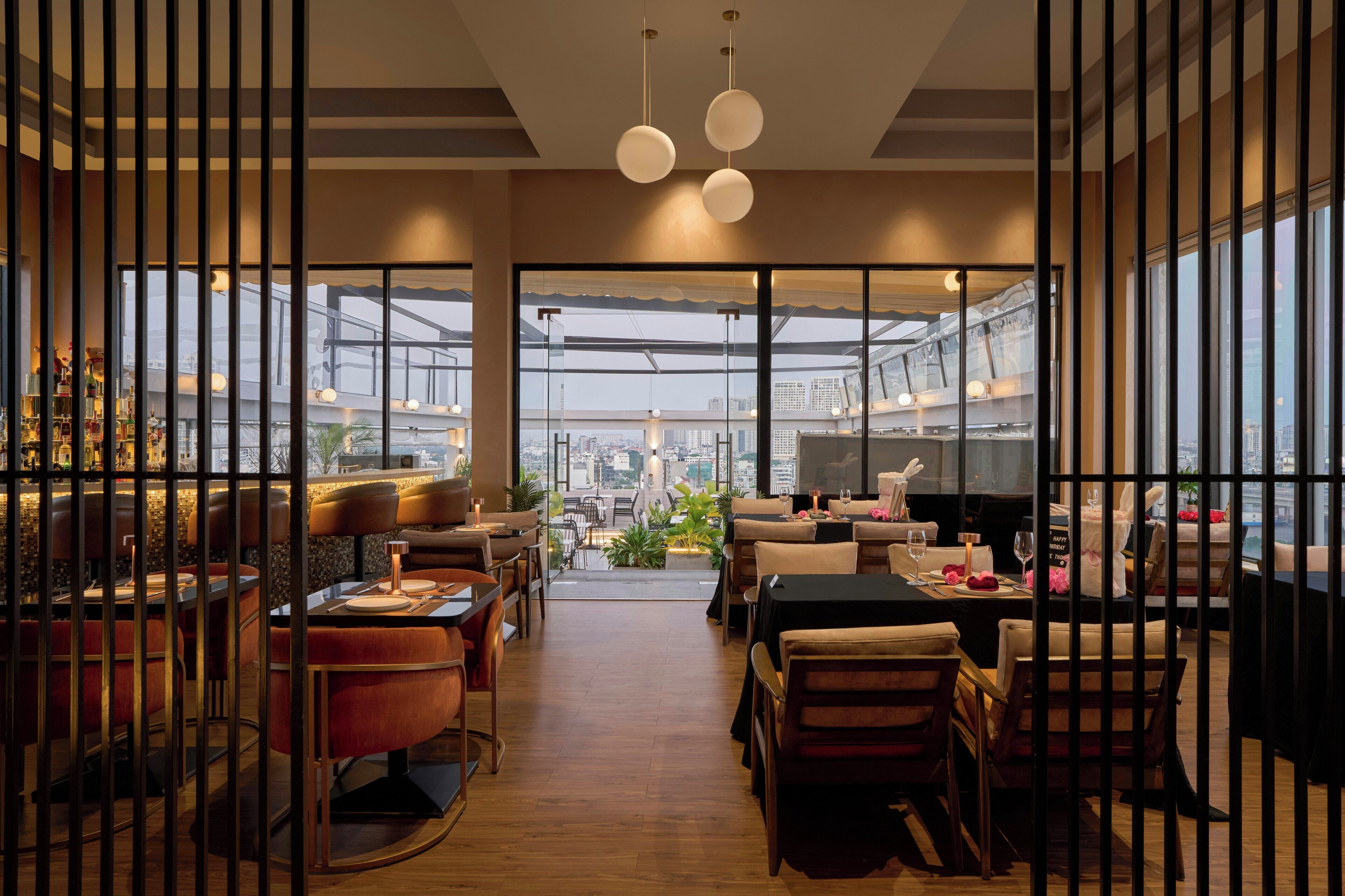 A modern restaurant with a view of the cityscape through large windows, wooden flooring, and contemporary furniture.