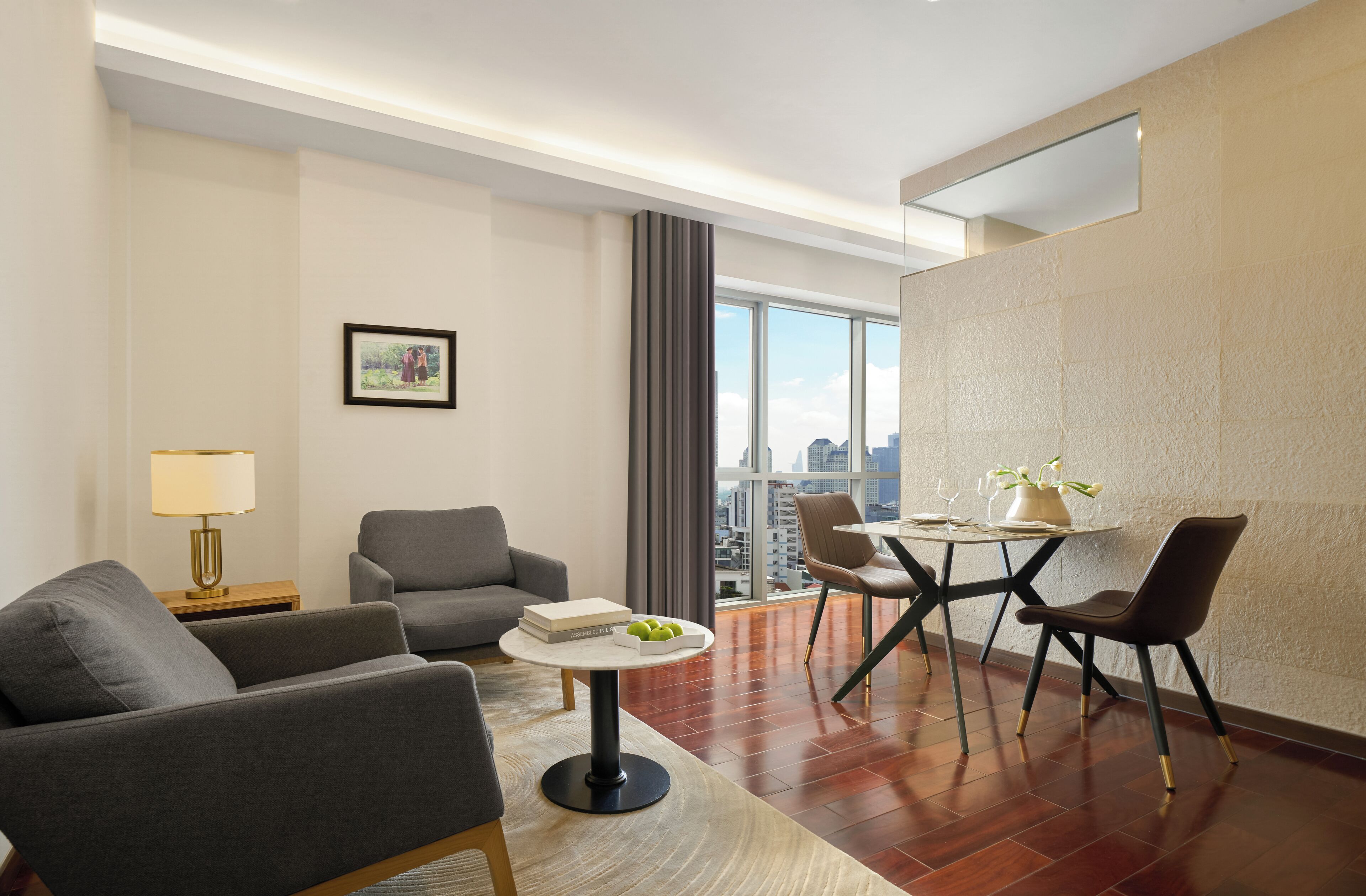 A modern hotel room with a sofa, dining table, and chairs, a city view, and a large window.
