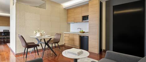 A modern kitchen with wooden cabinets, a built-in microwave, and a dishwasher. There is a dining area with a round table and chairs, and a living area with a sofa and a coffee table.