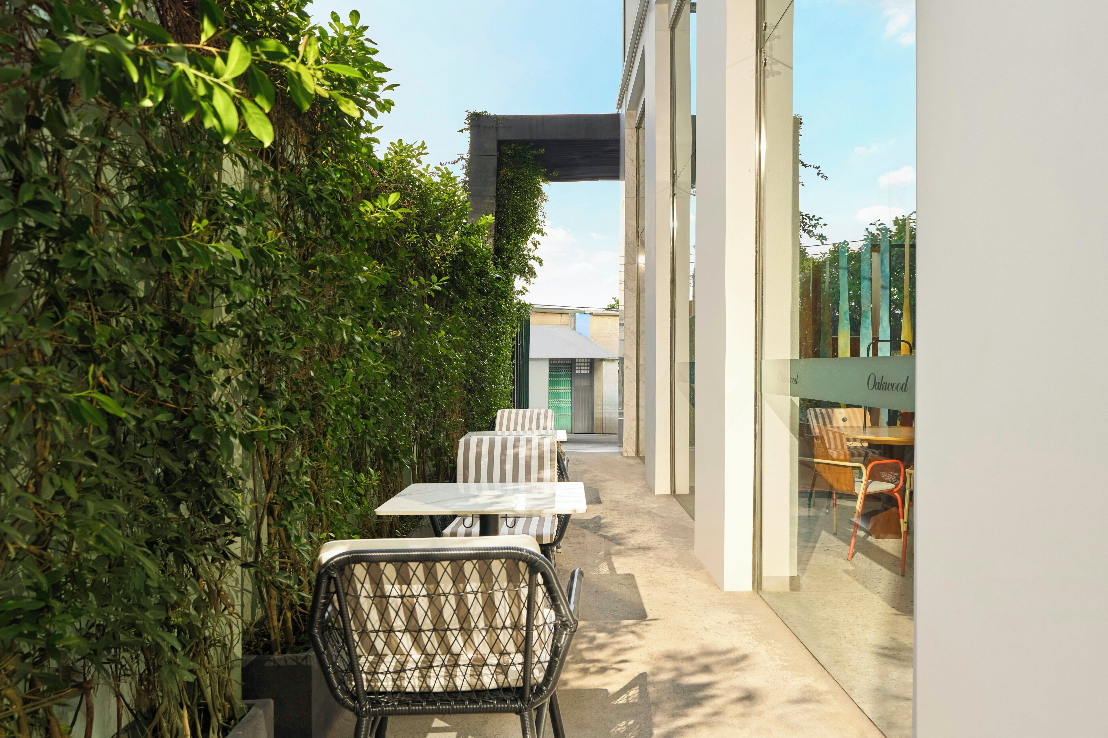 An outdoor patio with tables and chairs, a glass wall, and a view of a building with a green door.