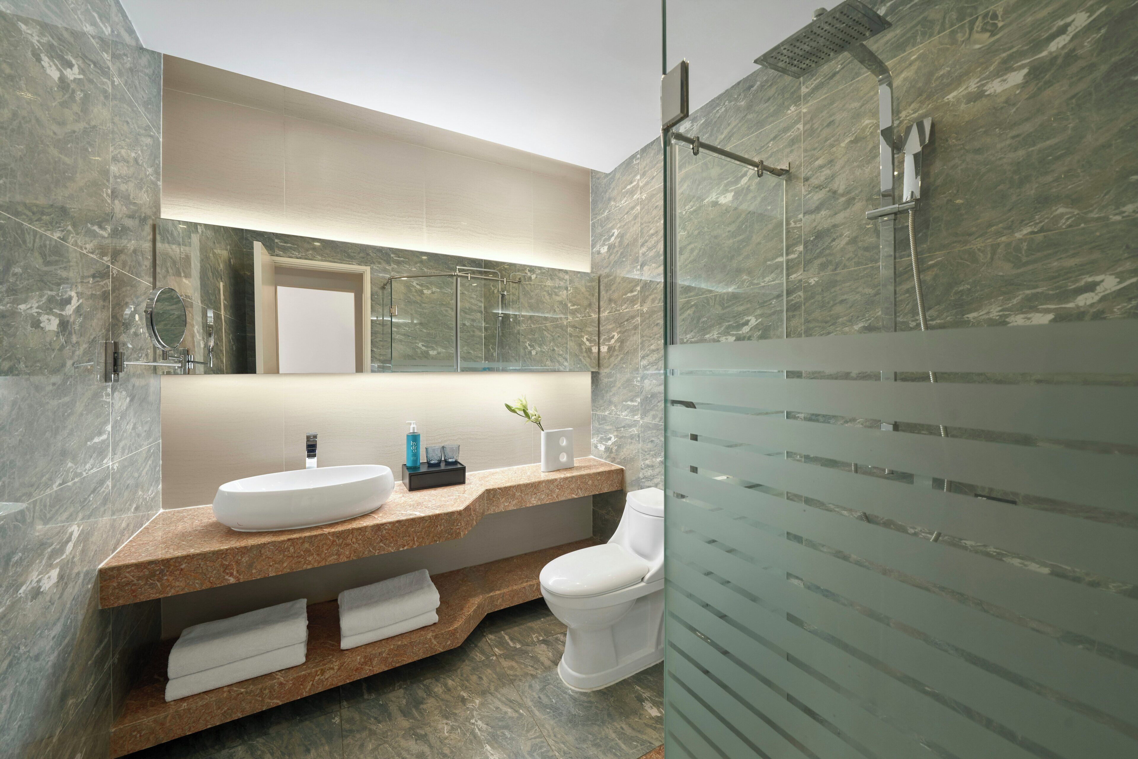 A modern bathroom with a marble vanity, a toilet, and a glass-enclosed shower area.