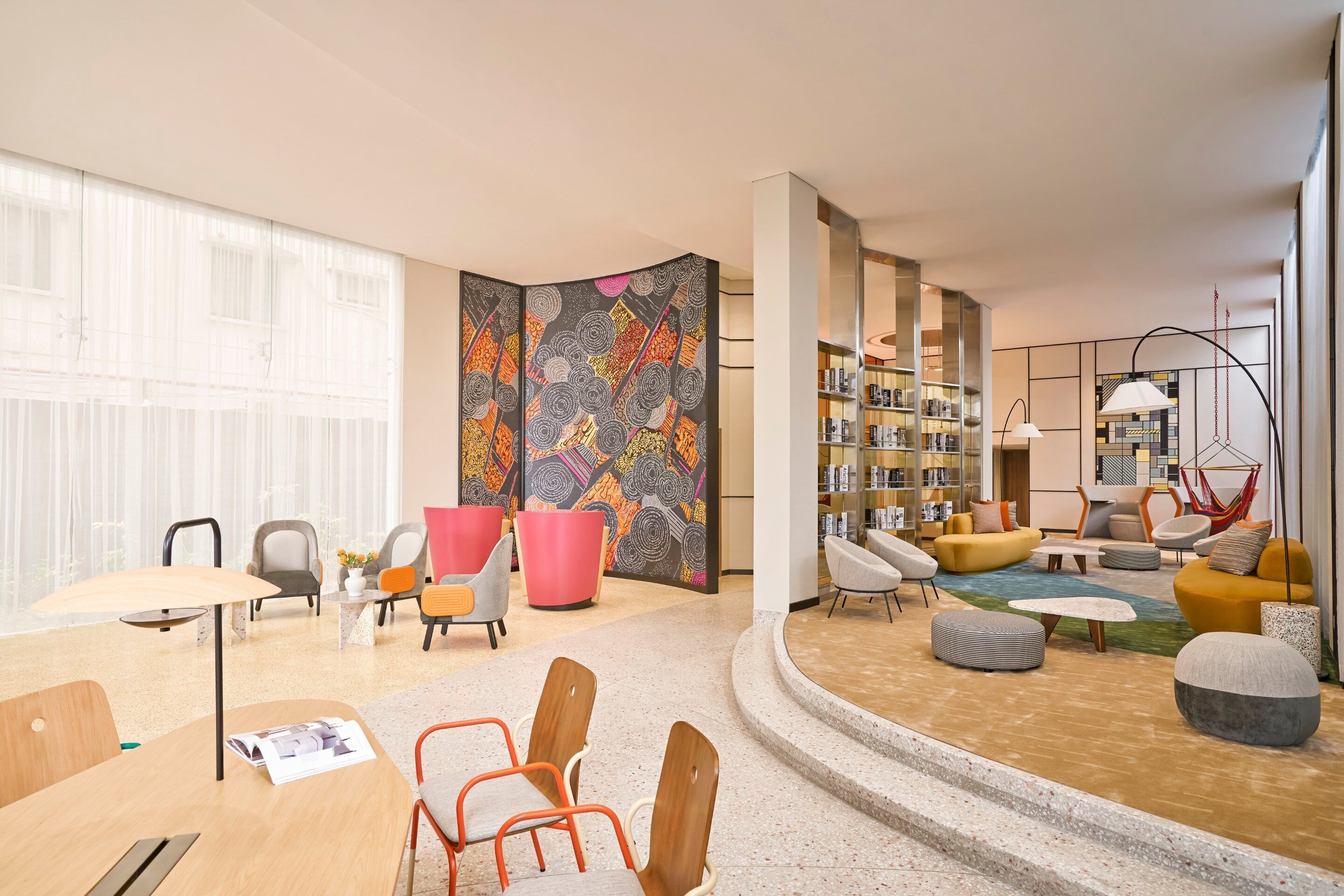 A modern lounge area with seating, a bookshelf, and a large window.