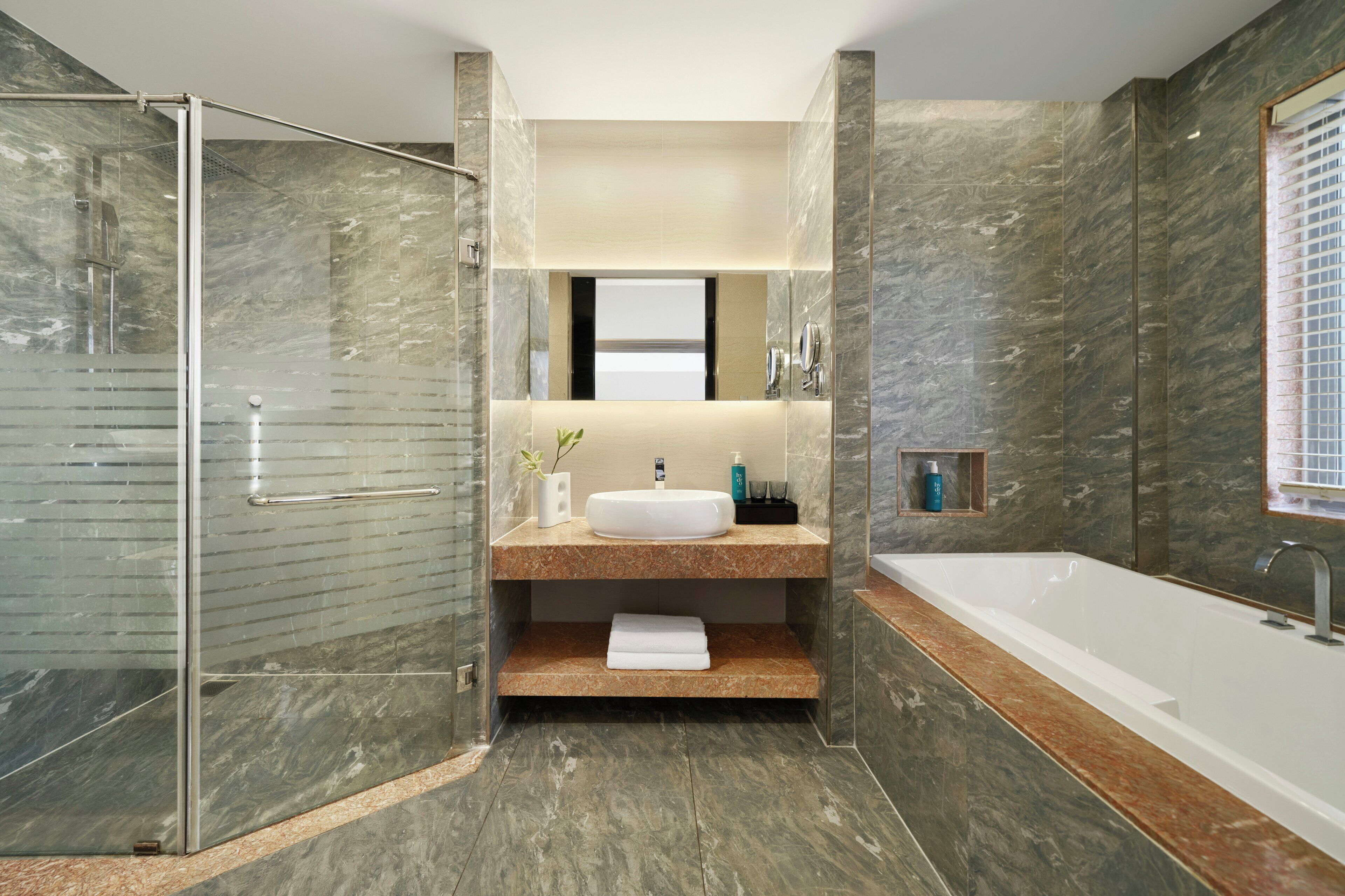 Une salle de bain moderne dotée d’une douche à parois de verre, d’un meuble-lavabo en marbre et d’un espace baignoire séparé.
