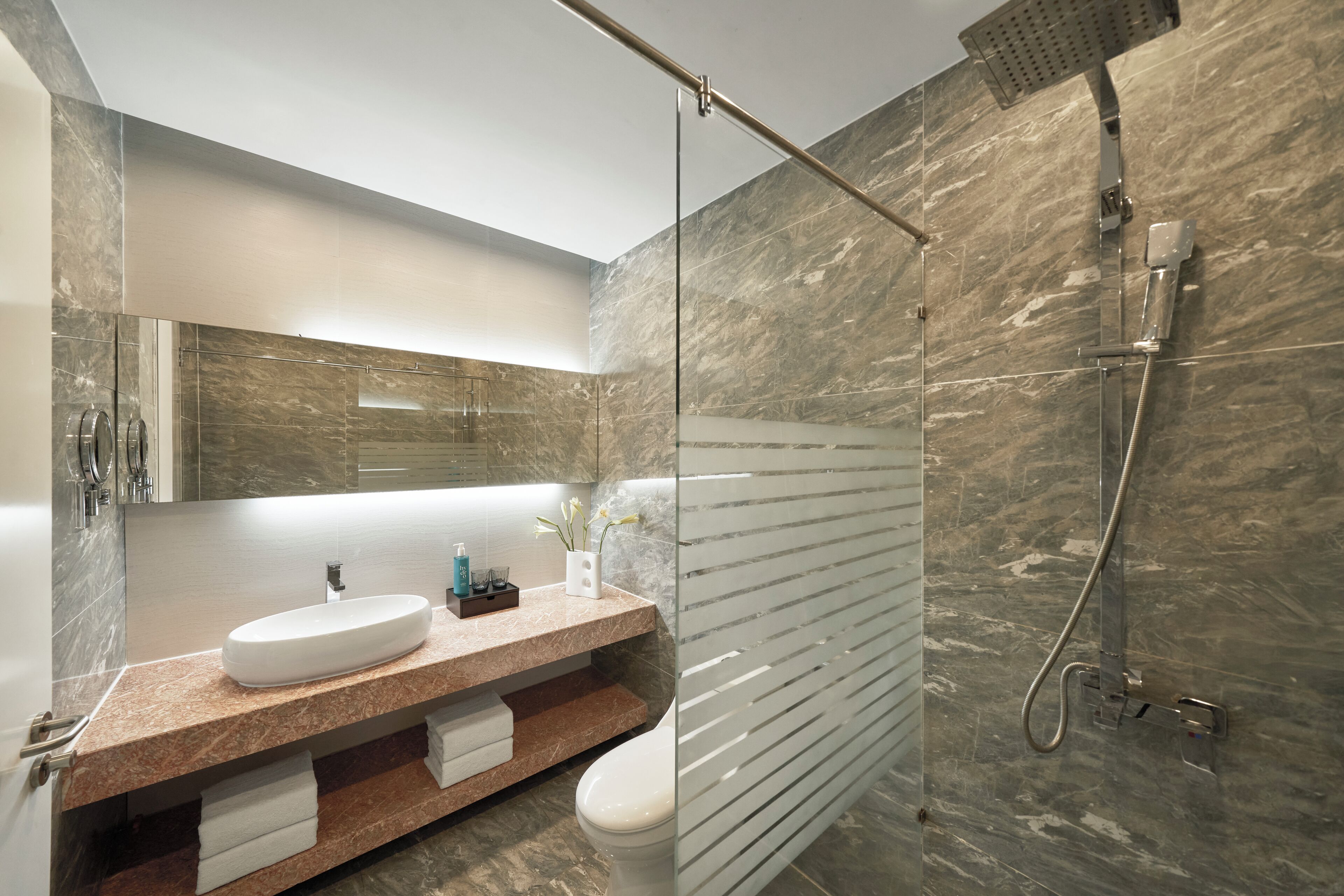 A modern bathroom with a glass-enclosed shower, a marble-tiled wall, and a vanity with a sink and towel rack.