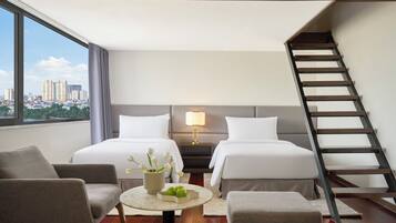 A hotel room with two beds, a sitting area with a table and chairs, a nightstand with a lamp, and a view of the city through large windows.