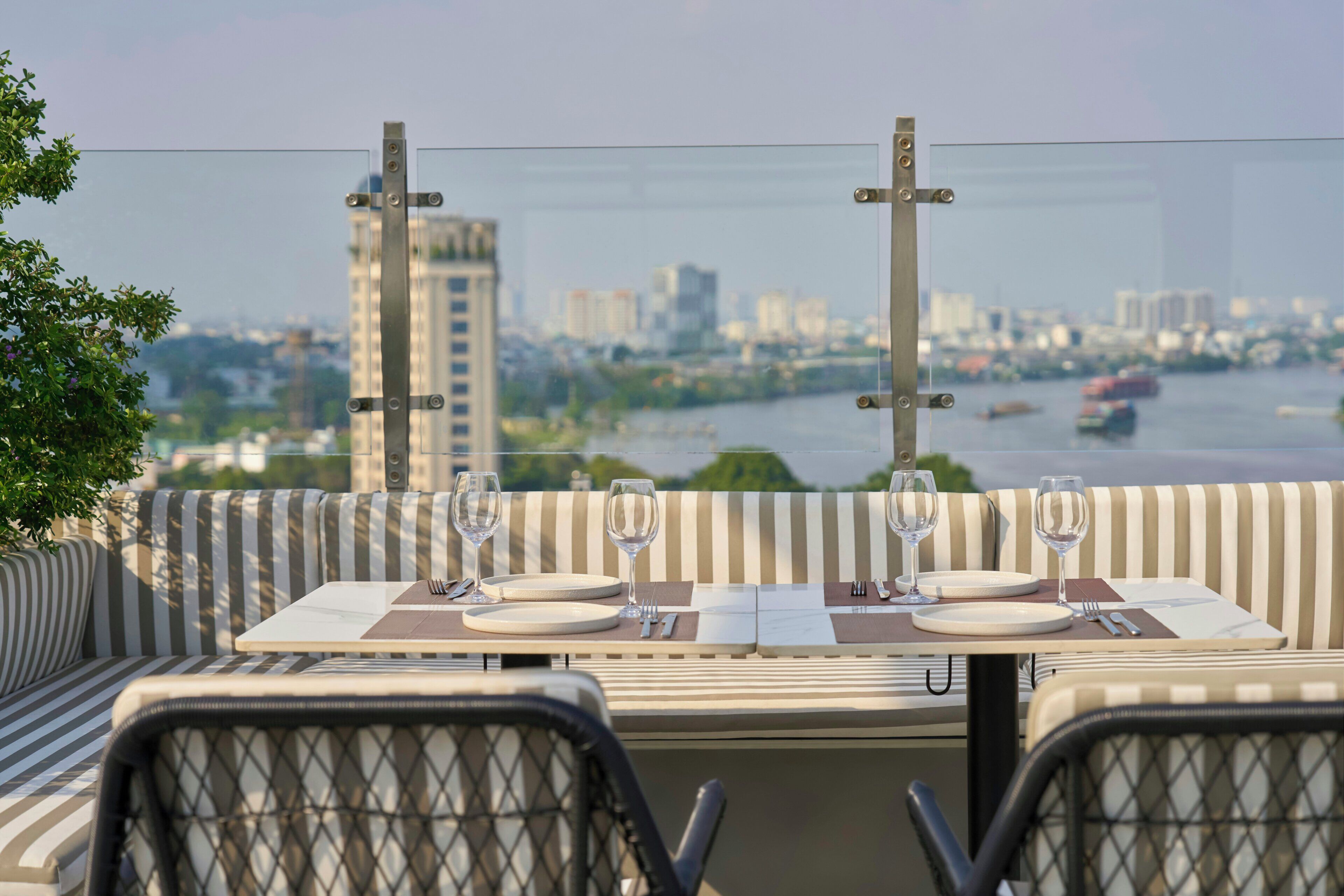 A dining area with a table set for two, overlooking a river with buildings in the background.