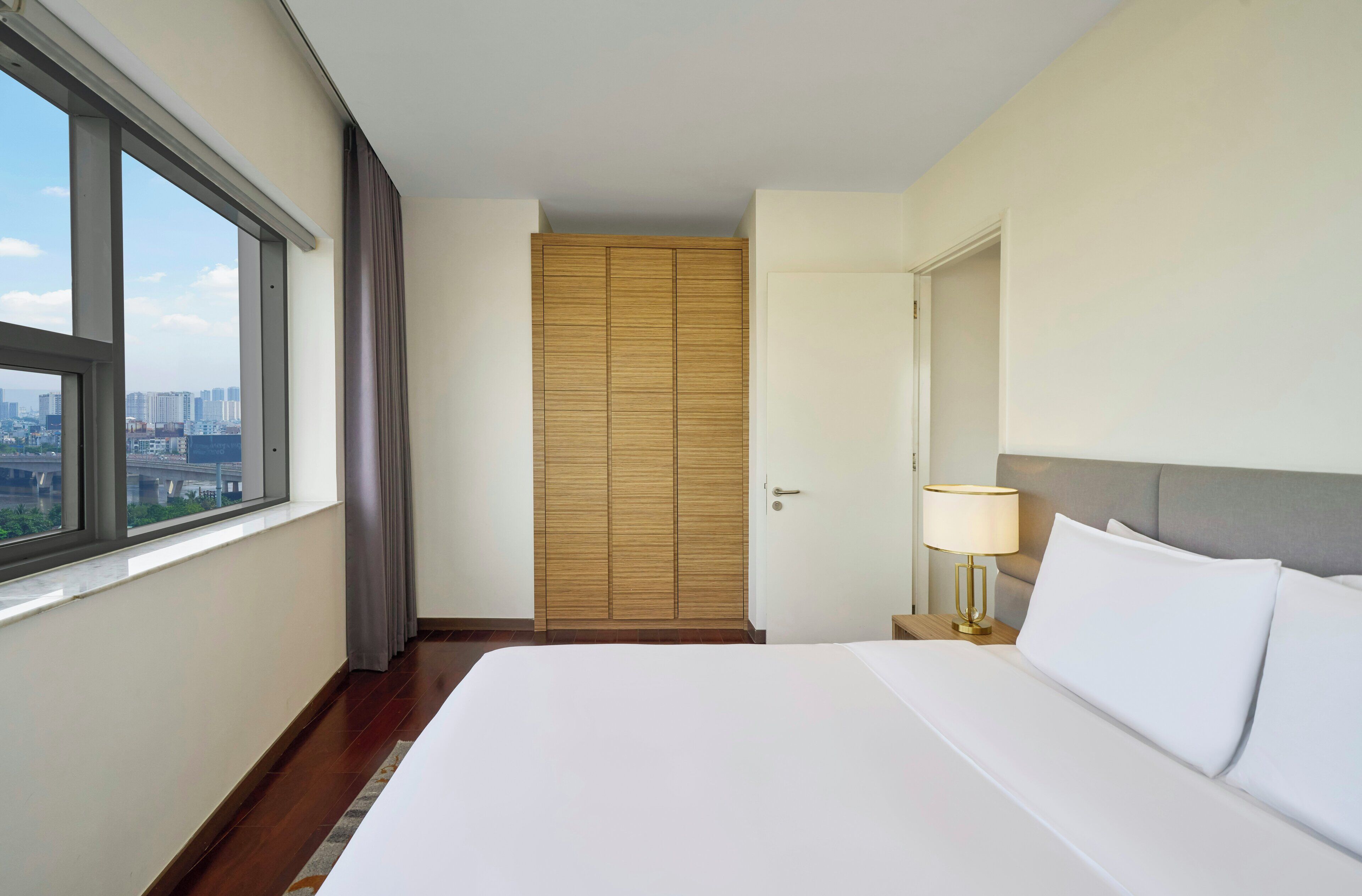 Hotelkamer met groot bed, nachtkastje met lamp, garderobe en raam met uitzicht op de stad.
