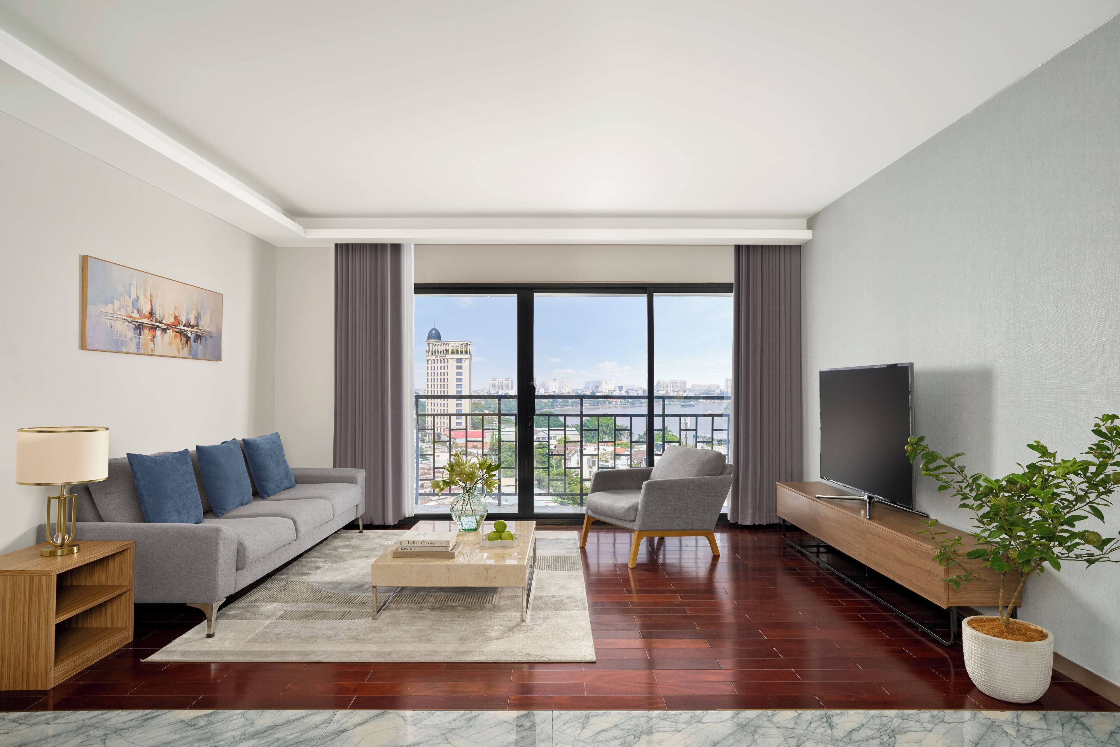 Un moderno salón con sofá, sillón, televisor y un amplio ventanal con vista a la ciudad.