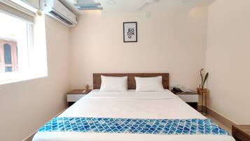 A hotel room with a bed, bedside tables, a ceiling fan, an air conditioning unit, a framed quote on the wall, and a window with a view of a building.