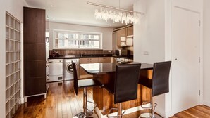 A modern kitchen with a central island, bar stools, and a chandelier.