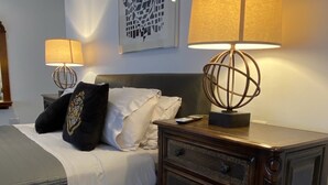 A neatly arranged bedroom with a bed, bedside lamps, a dresser, and an air conditioning unit.