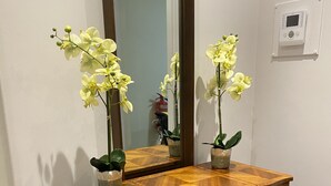 A wooden vanity with two potted orchids, a mirror, and a wall-mounted thermostat.