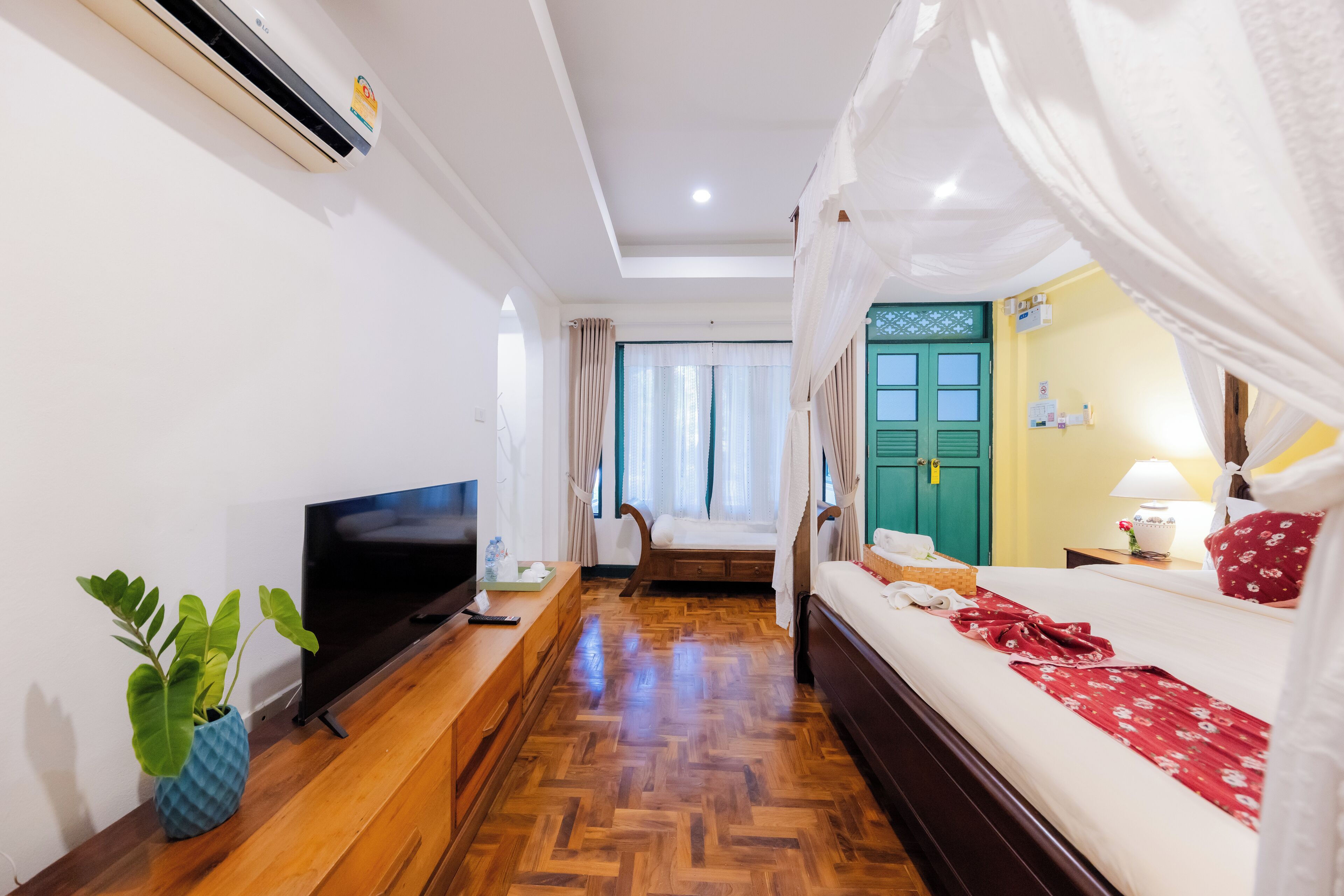 Habitación de hotel con suelo de madera, televisor, mesita de noche con lámpara, cama con dosel y puerta verde.