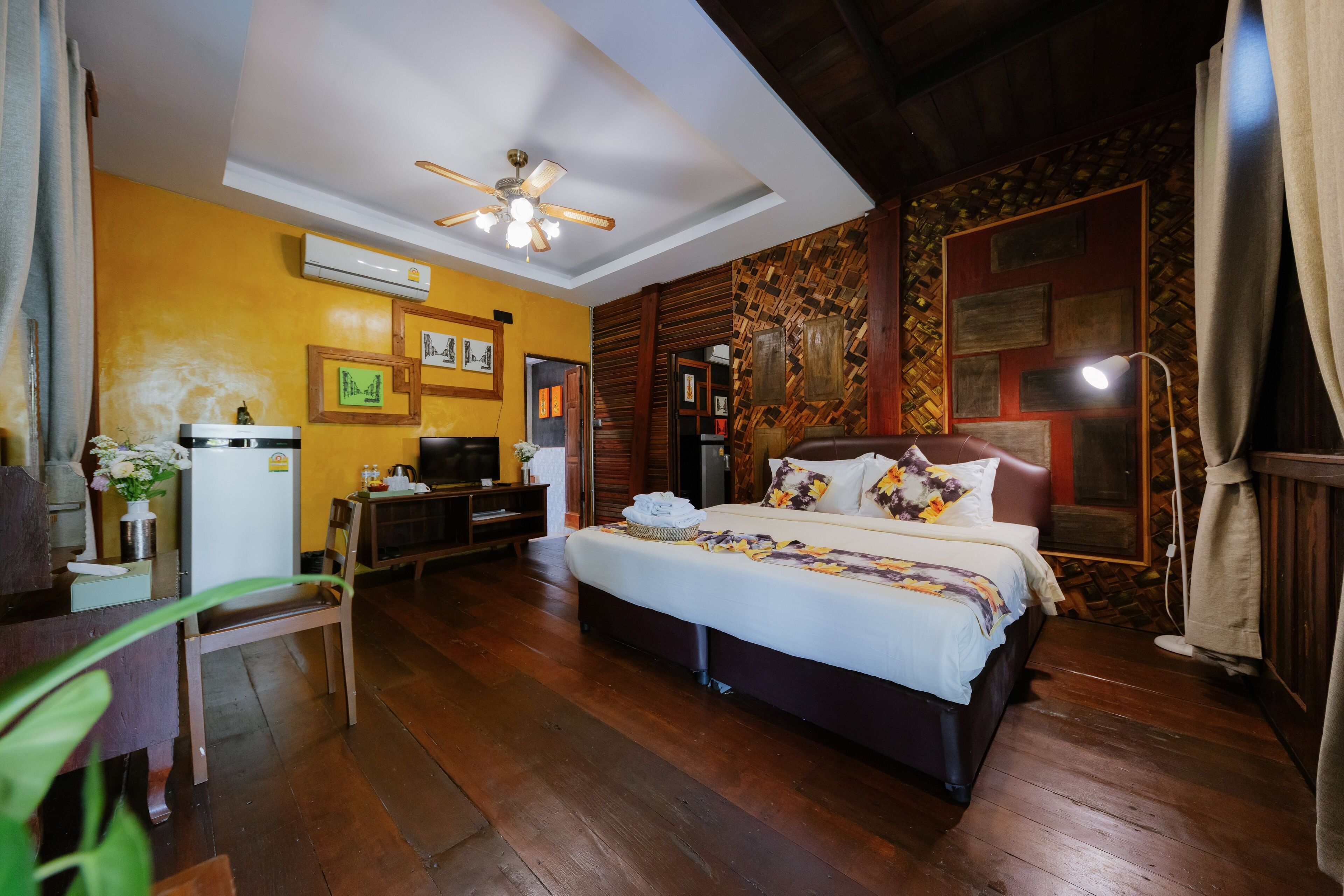 A hotel room with a bed, a desk, a chair, a ceiling fan, and a wall-mounted air conditioner.