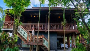 A wooden structure with a balcony and stairs, surrounded by tropical vegetation. - Teewana Resort Chiang Mai (Hang Dong)