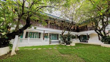 A two-story building with a white exterior, green shutters, and a balcony with a railing.