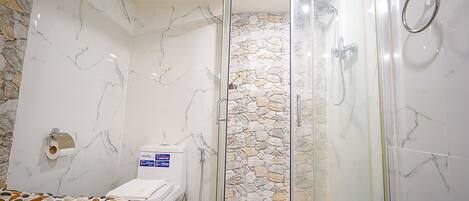 A bathroom with a shower, toilet, and a bed with a patterned cover.