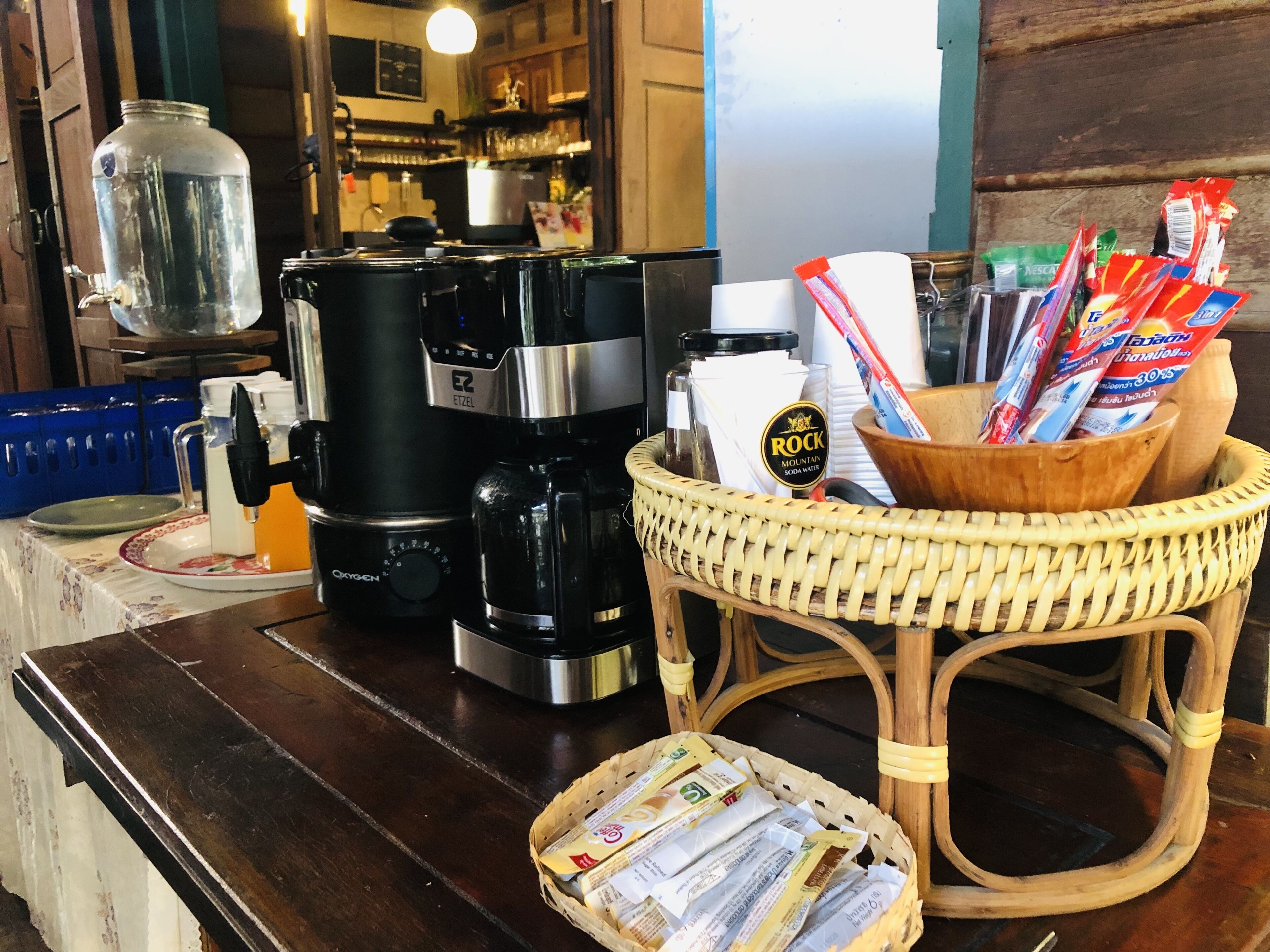 A coffee station with a coffee maker, a water dispenser, and a basket of newspapers.