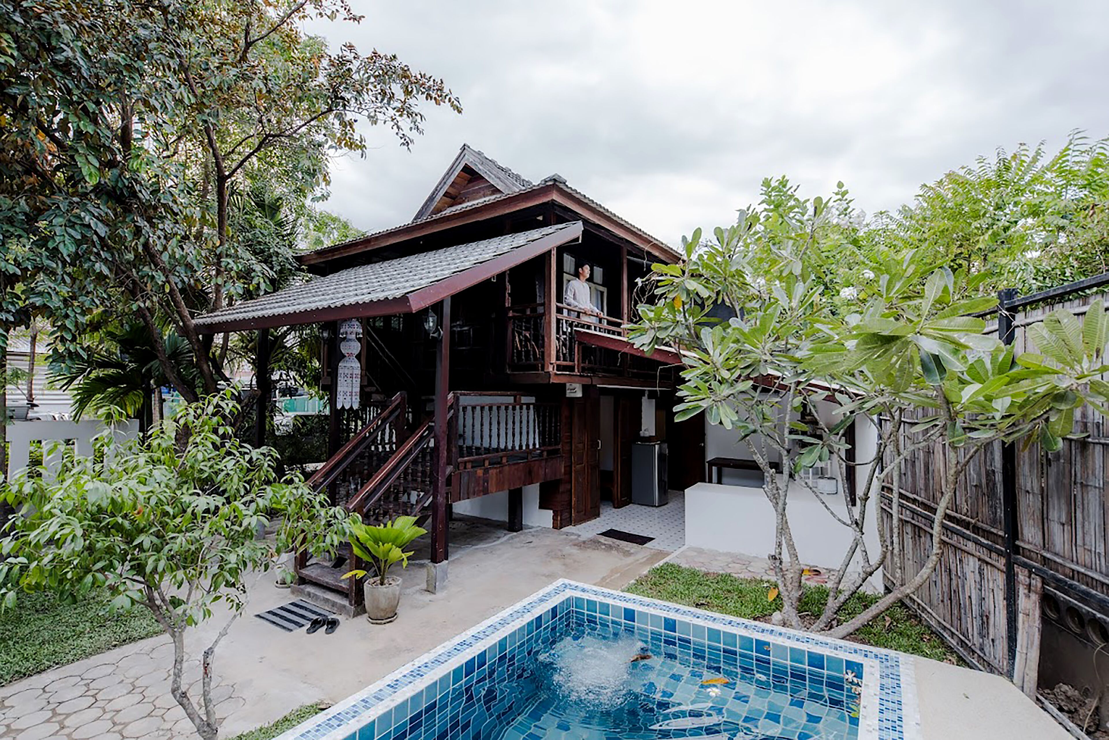 A wooden house with a tiled pool, surrounded by greenery and a wooden fence.