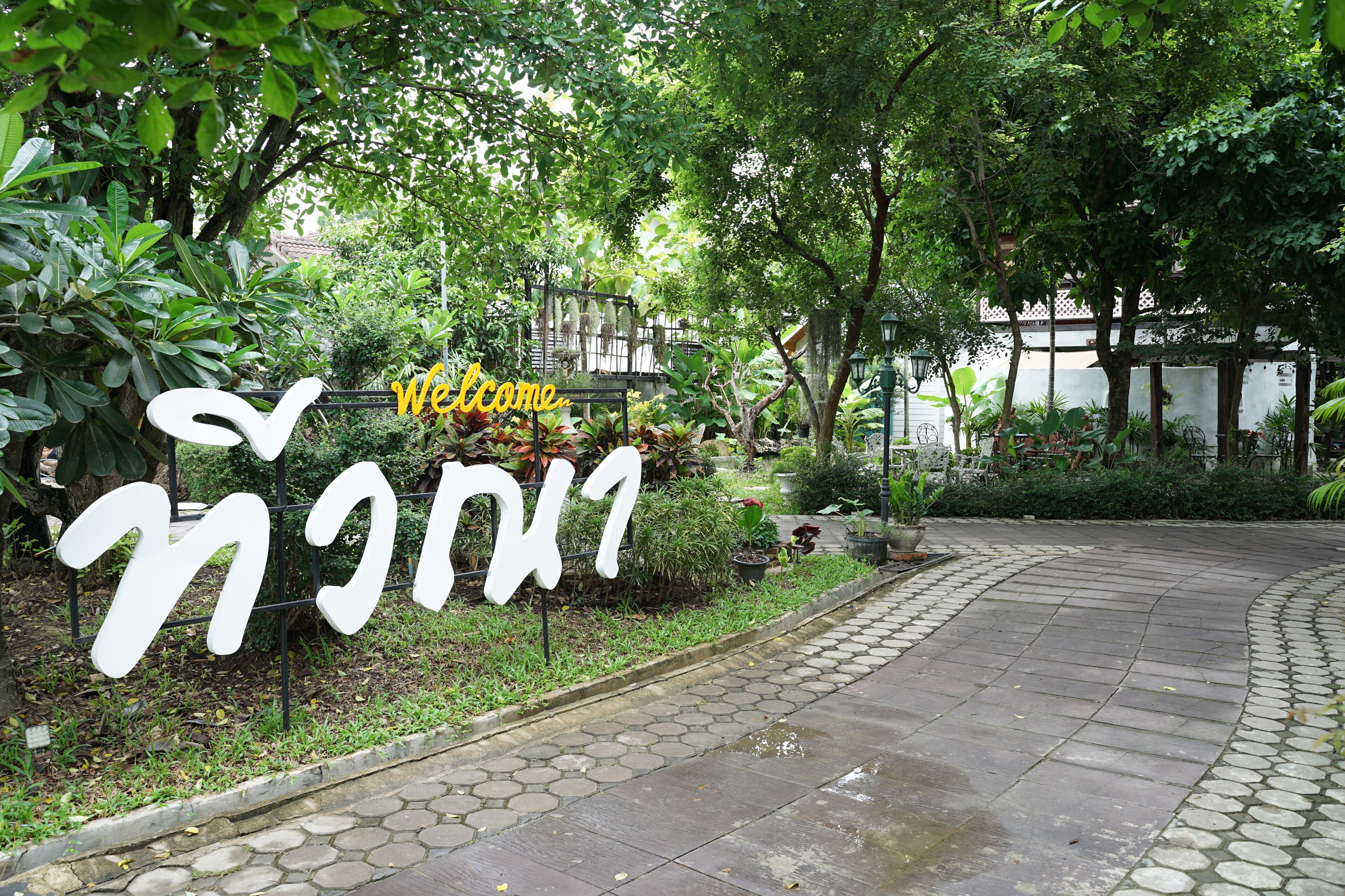 A garden entrance with a sign that reads "Welcome" and "มิตรภาพ" in Thai script.