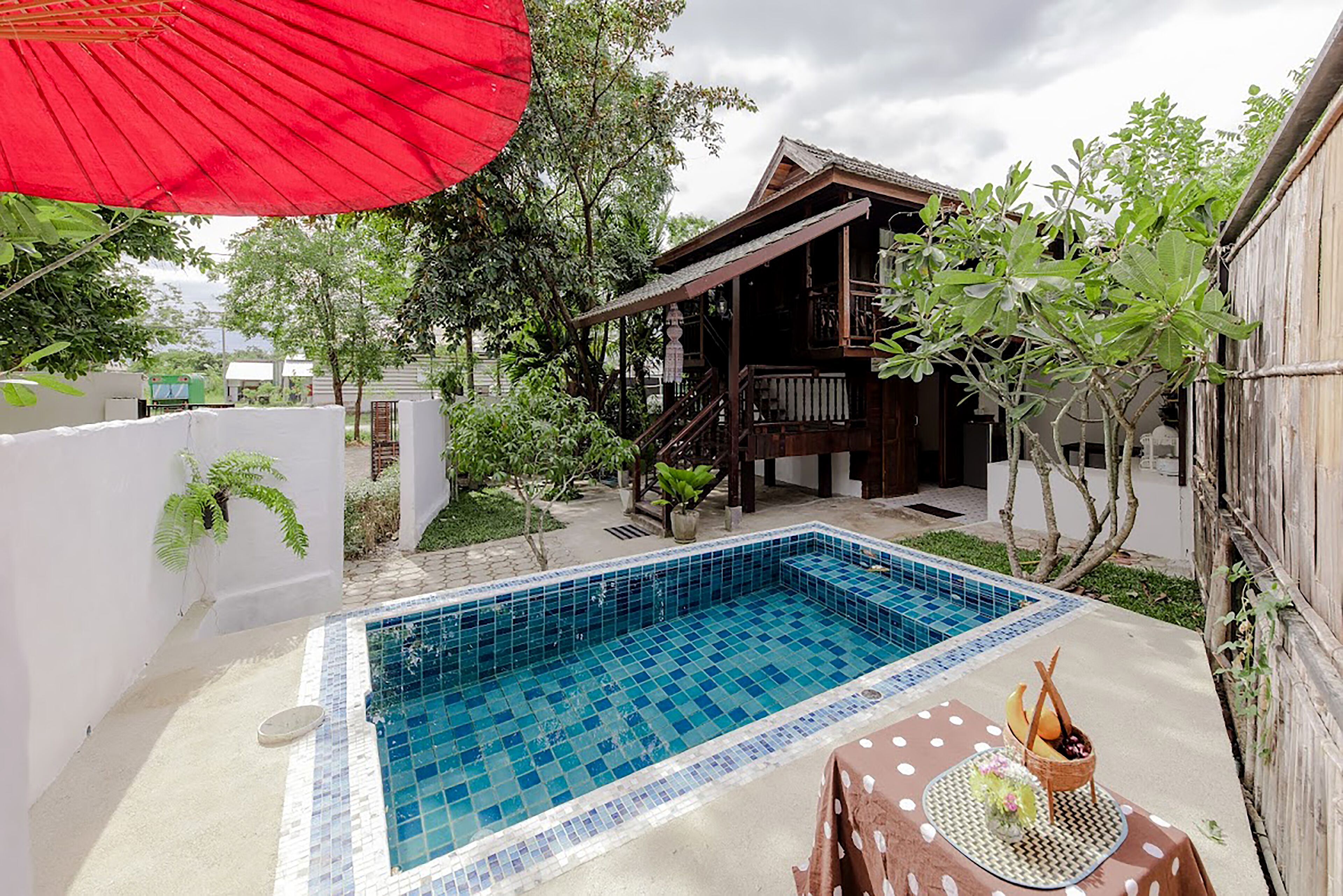 Une piscine dotée d’une plage carrelée, entourée d’une terrasse en bois et d’un petit espace de repos couvert.