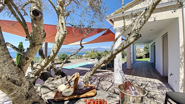 En terrasse med et træbord dækket til et måltid, en pool og udsigt til havet og bjergene.