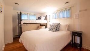 A bedroom with a bunk bed, a single bed, a bedside table, and a window with curtains.