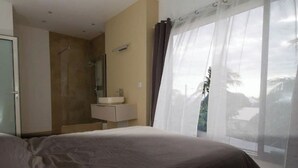 Een hotelkamer met een bed, een badkamer met douche, wastafel en een groot raam met gordijnen.