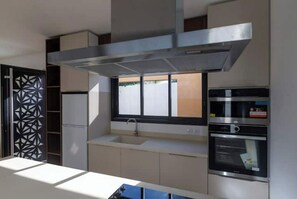 A modern kitchen with a stainless steel range hood, a built-in oven, and a window above the sink. - Villa Opale (Saint-Pierre)