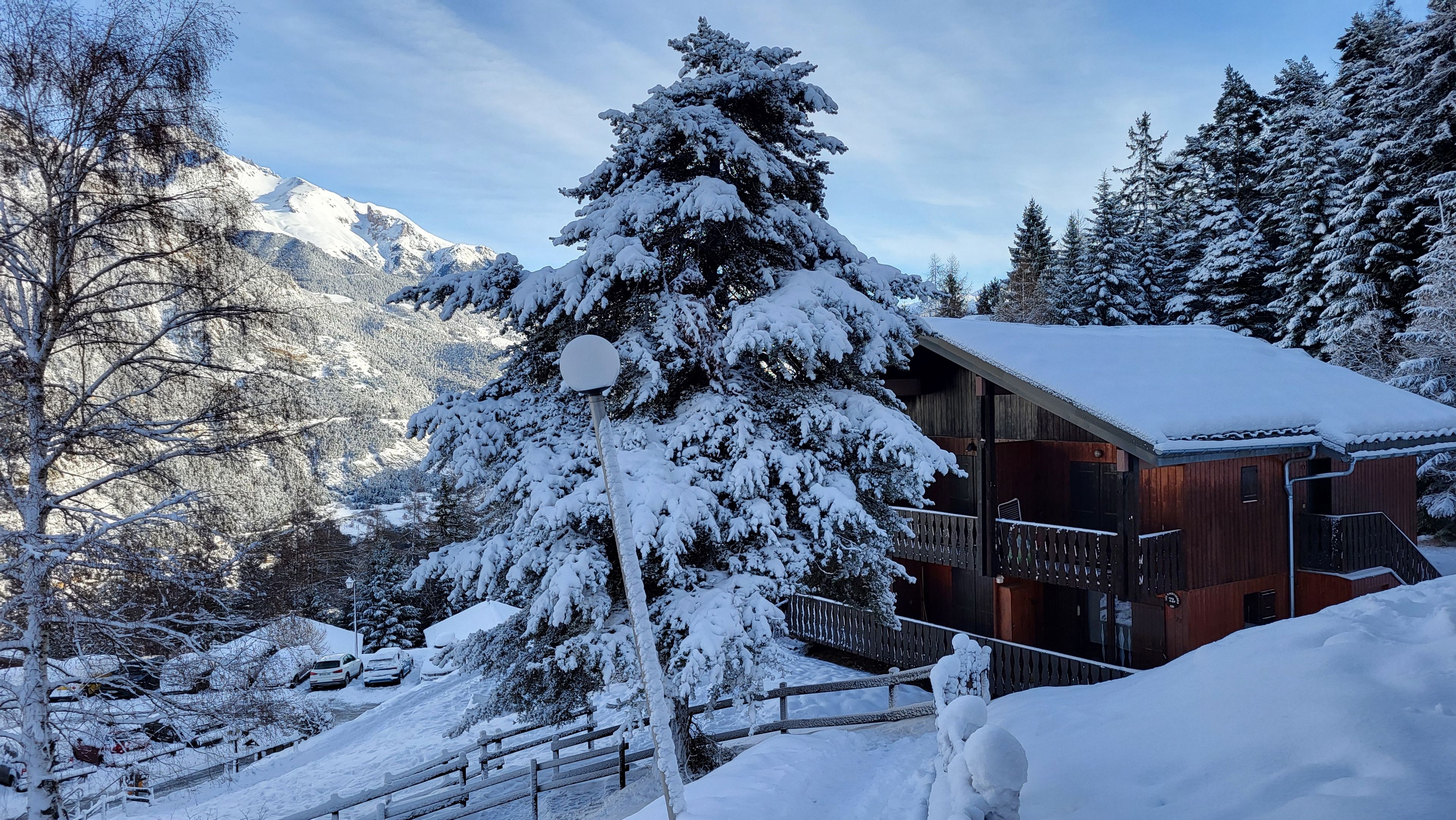 A snow-covered mountain lodge with a wooden exterior, a balcony, and a view of the surrounding snowy landscape.