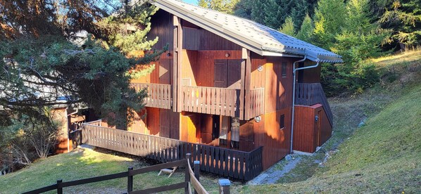 Una cabaña de madera con balcón, rodeada de árboles y una pendiente cubierta de hierba.