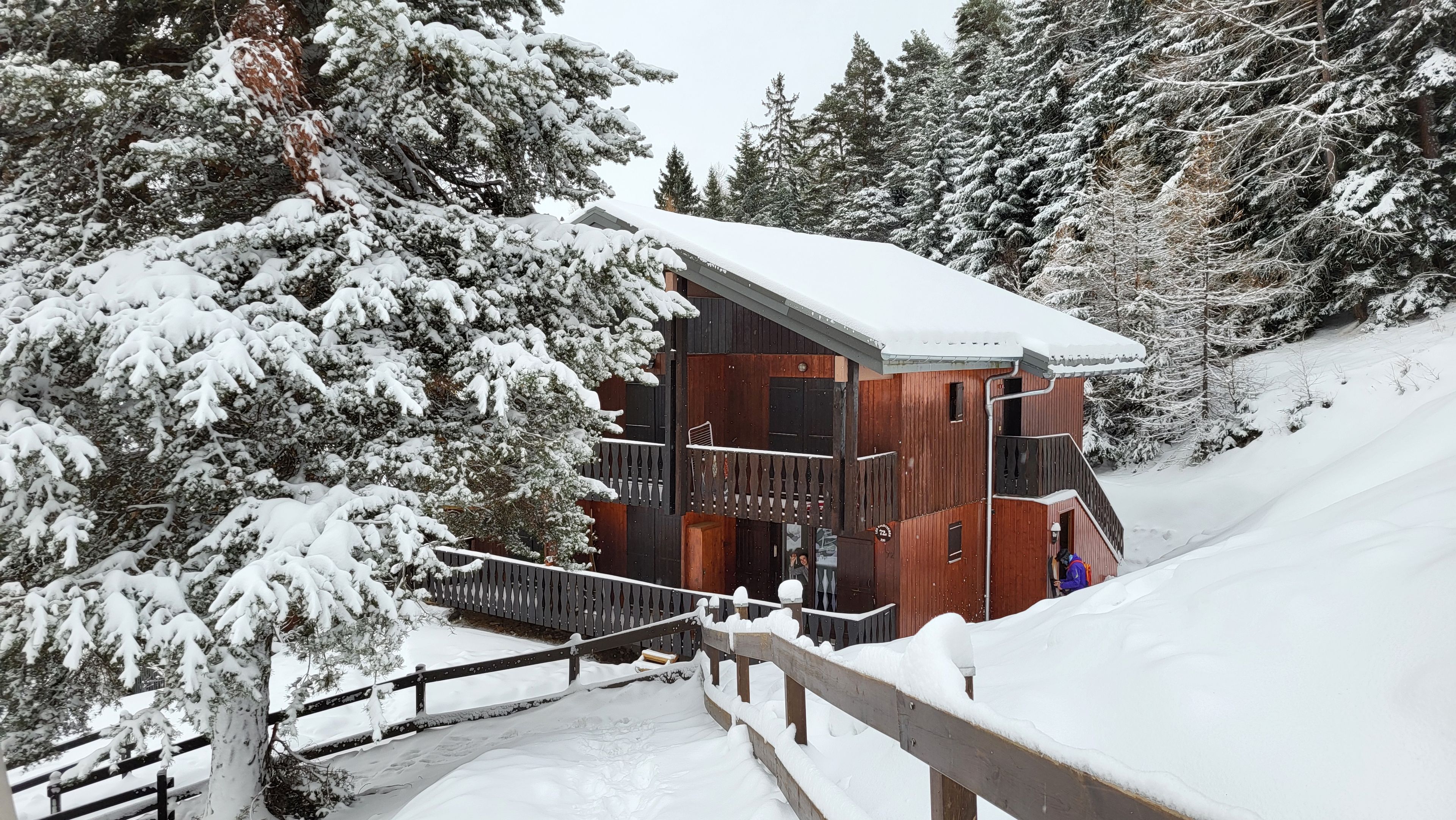 Eine Holzhütte mit einem Balkon, umgeben von schneebedeckten Bäumen.