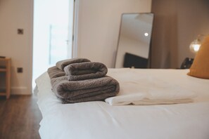 A neatly made bed with folded towels and a large mirror on the wall.
