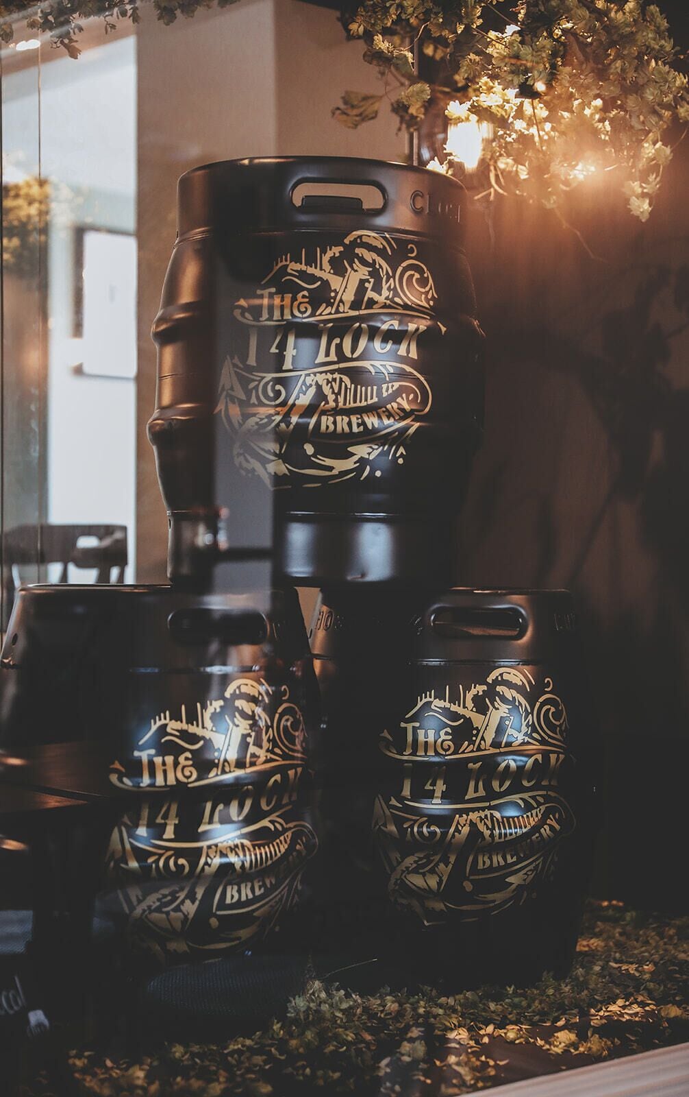 Three kegs with 'The 14 Lock Brewery' branding, placed on a table with a glass window in the background.