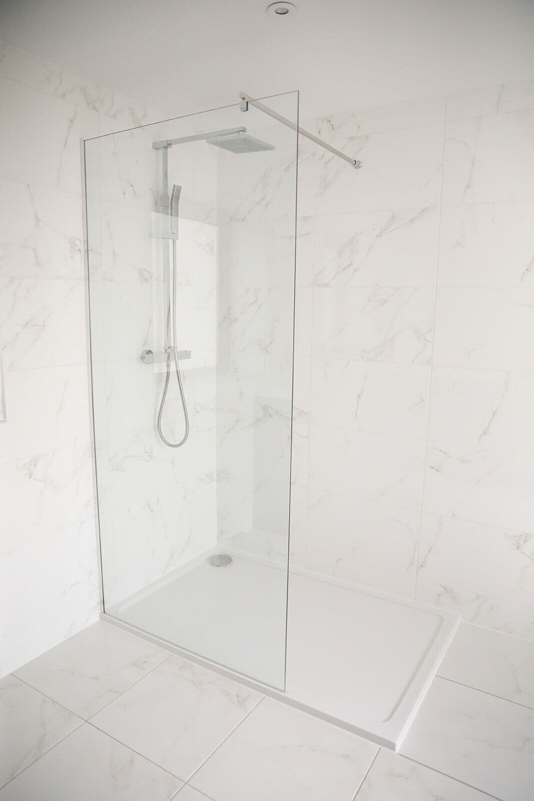 A glass-enclosed shower with a handheld showerhead and a fixed showerhead.