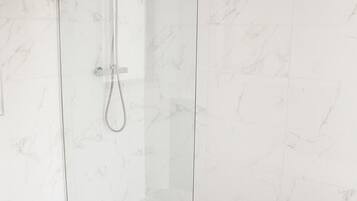 A glass-enclosed shower with a handheld showerhead and a fixed showerhead.