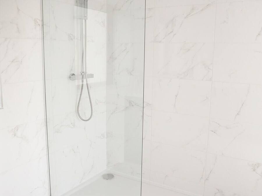 A glass-enclosed shower with a handheld showerhead and a fixed showerhead.