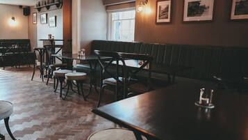 Interior acogedor de un restaurante con mesas y bancos de madera, cuadros en las paredes y un suelo con estampado tipo espiga.