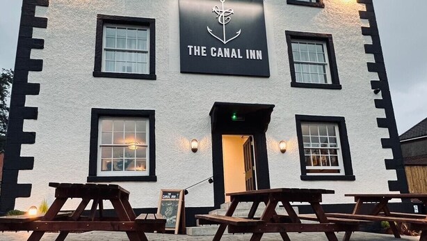 A building with a sign reading "The Canal Inn" and a logo of an anchor. There are picnic tables in front. - The Canal Inn (Belper)