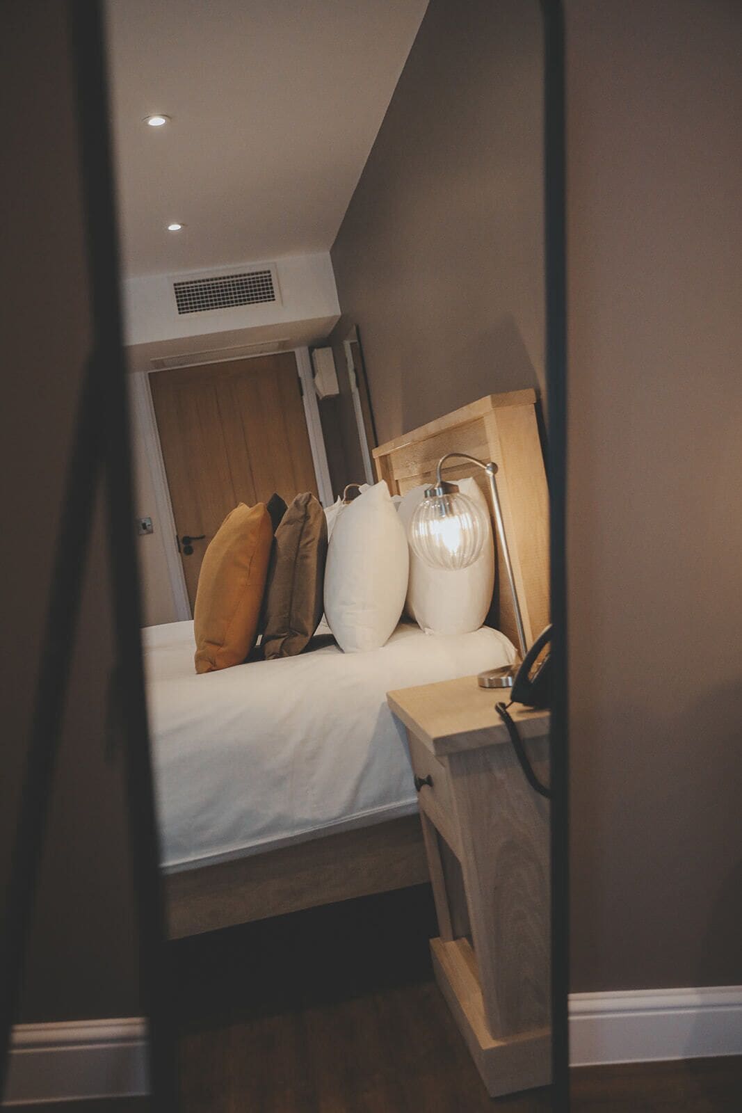 Un dormitorio con cama, almohadas, mesita de noche y lámpara.