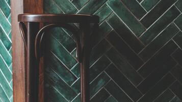 A bar stool in a room with a herringbone-patterned green tile backsplash and wooden flooring.