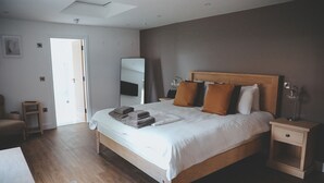 A bedroom with a wooden bed, a bedside table, a nightstand, a mirror, and a door leading to another room. - The Canal Inn (Belper)