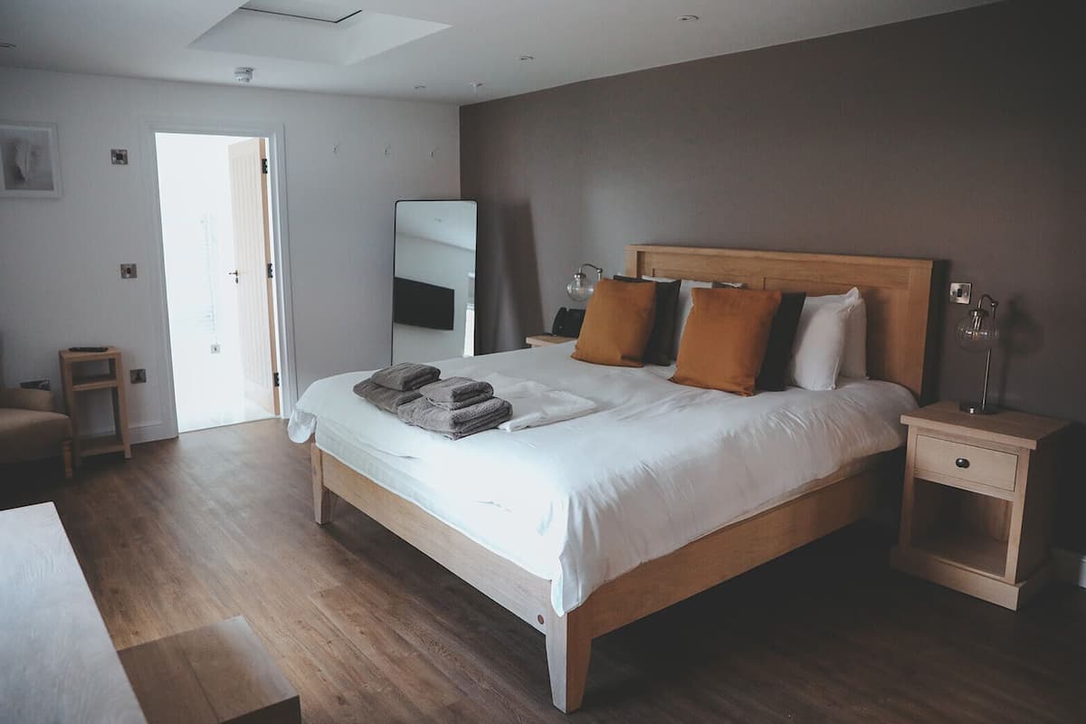 A bedroom with a wooden bed, a bedside table, a nightstand, a mirror, and a door leading to another room.