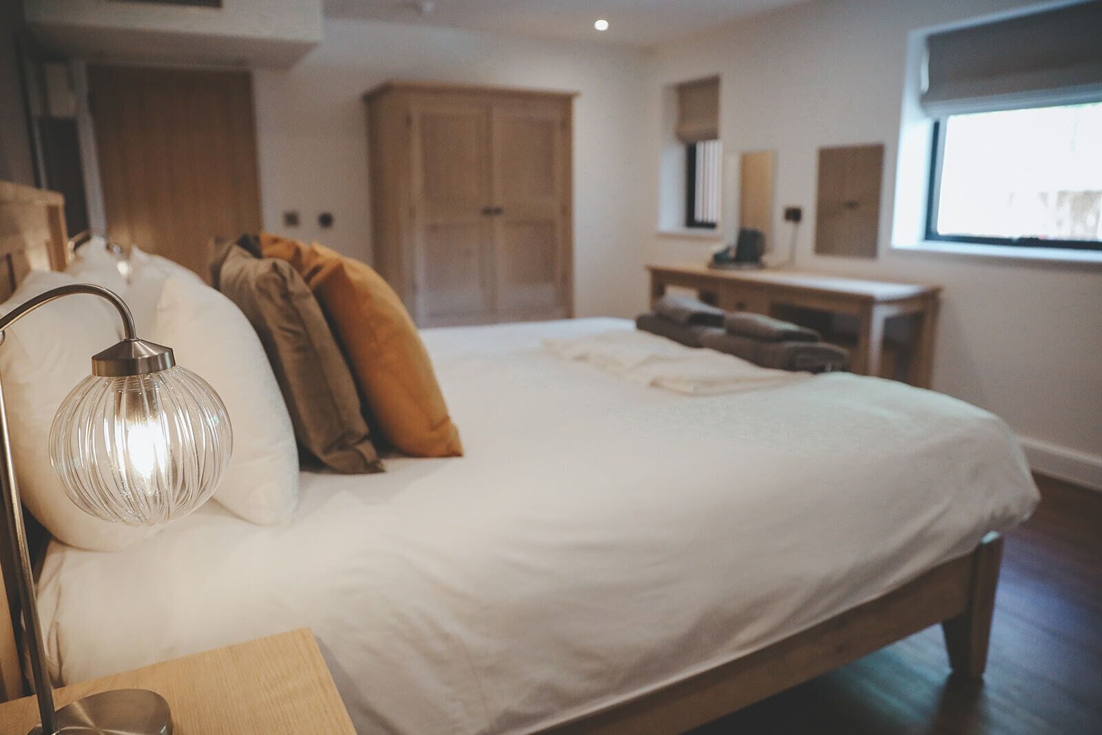 A bedroom with a large bed, a bedside lamp, a wooden nightstand, and a wardrobe.