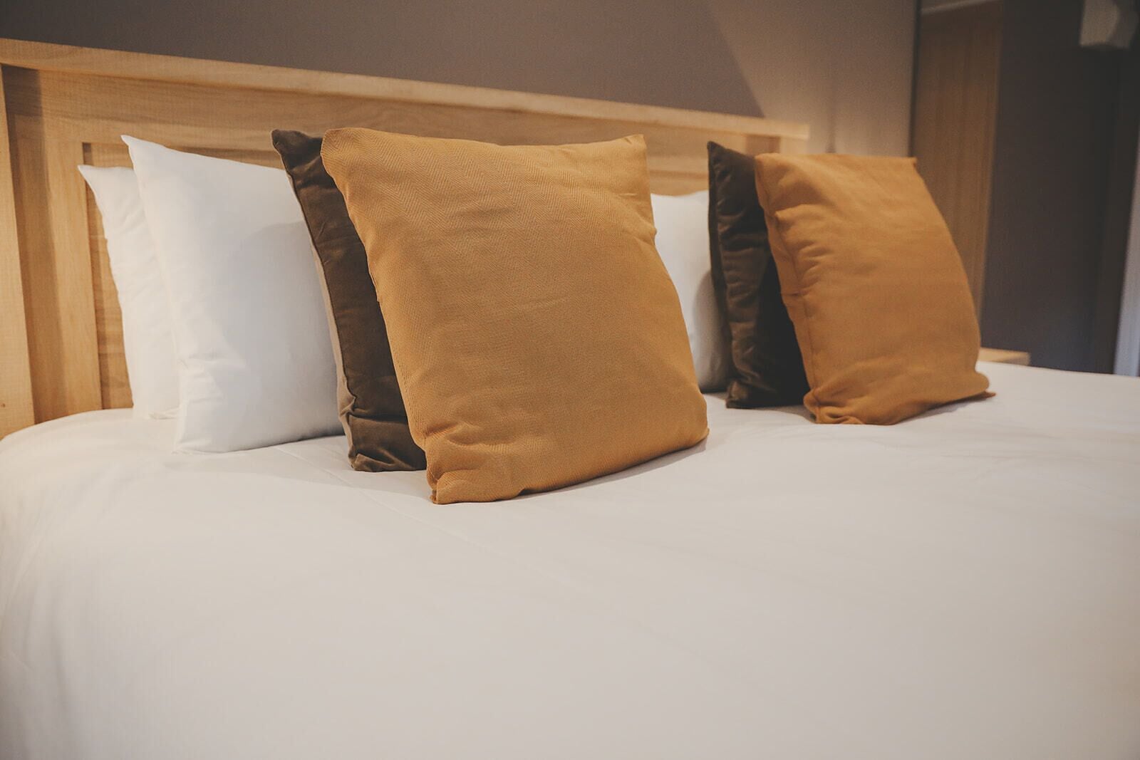 Un lit avec des oreillers blancs et de couleur moutarde, une tête de lit en bois et un couvre-lit blanc uni.