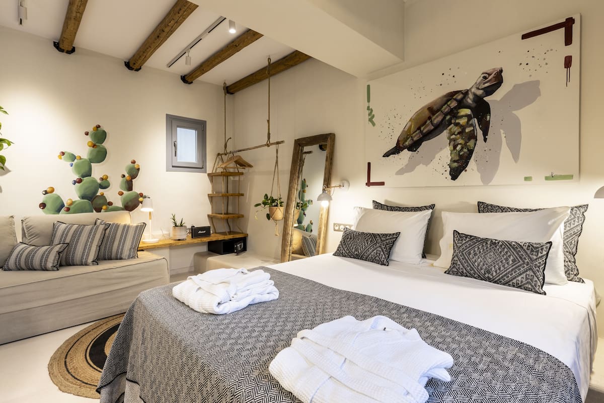 Un dormitorio con cama, almohadas, una mesita de noche, una planta colgante y un cuadro en la pared.
